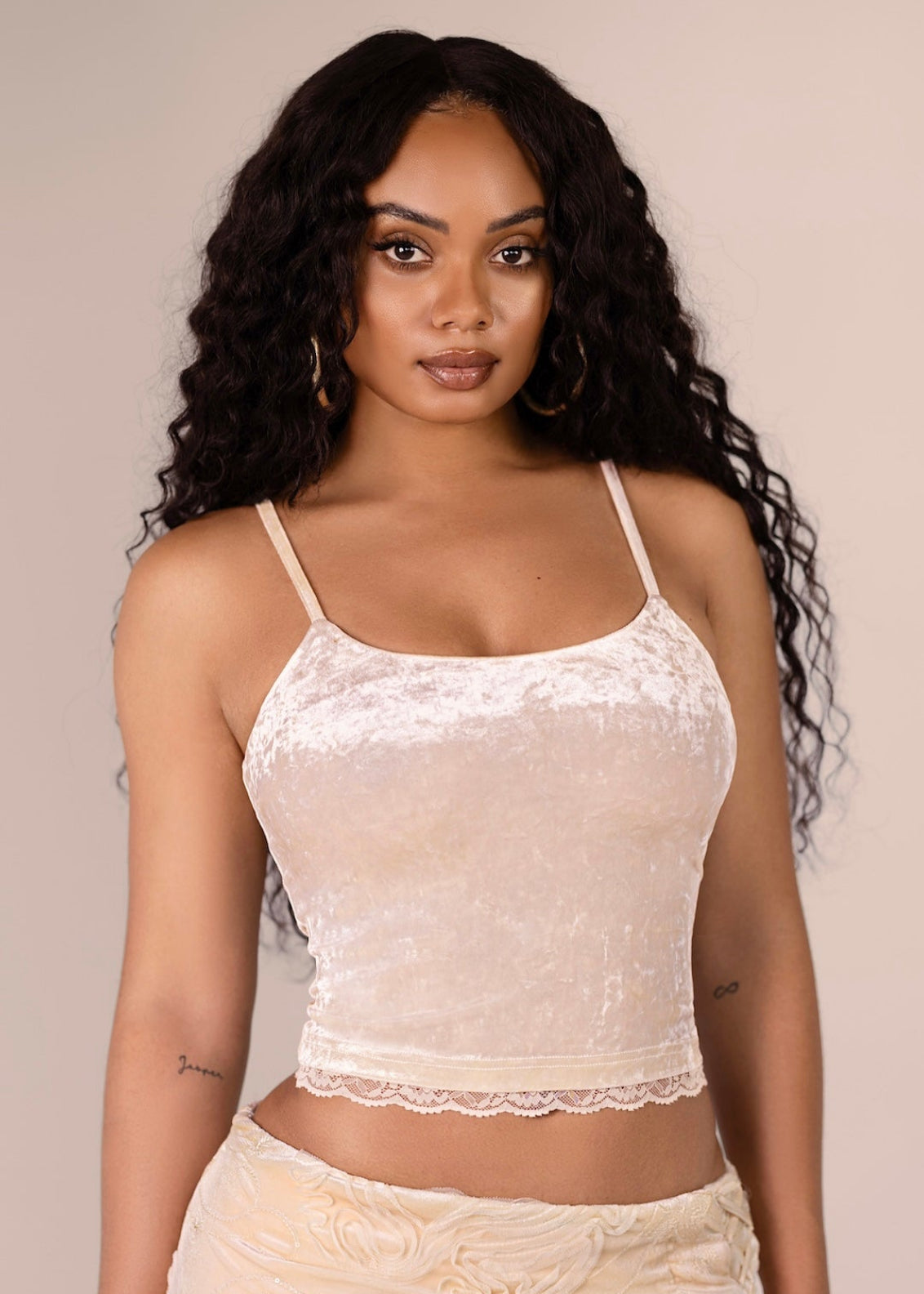 Woman wearing a beige lace top and skirt set against a plain background